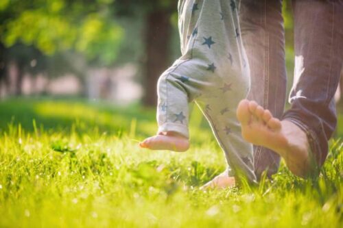 Parent and child walking on grass barefoot